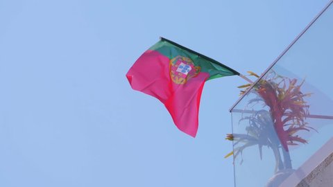 Portugal flag fixed on glass house balcony and fluttering on wind against blue sky