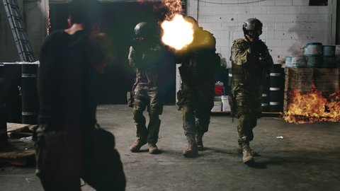 Playback movie or commercial of armed SWAT police team enter a warehouse that's on fire shooting bad guys from a gang with rifle guns with VFX. Wide shot on 4k RED camera.