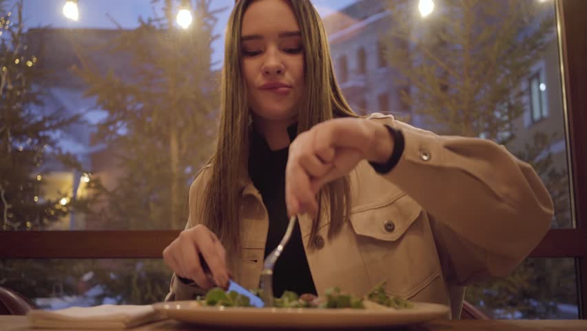 Pretty young girl eating salad using fork and knife close up. Lonely lady spend time out of home in restaurant or cafe