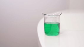A close-up of woman's hand in pink glove holding a measuring cup with green detergent - Powered by Shutterstock - Get 15% off with code: PIKWIZARD15