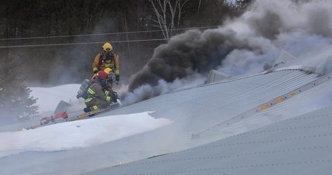 Quebec, Canada - February 2019 - Black smoke issuing from factory fire, firefighter spray water in the roof.