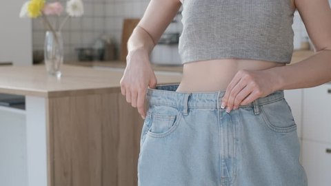 Slim woman body in big jeans. Healthy diet results. Young woman enjoy weight loss at home. Happy female in old jeans after successful diet indoors.Close up