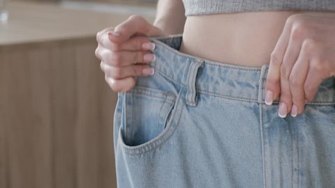 Slim girl in big oversized jeans. Happy female in old jeans after successful diet. Woman in jeans of the big size rejoices that as she lost weight thanks to healthy food and sports. Lifestyle. Closeup