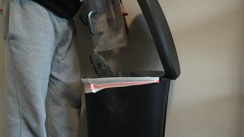 Man emptying full vacuum canister into a flip top garbage can and producing dust in the air
