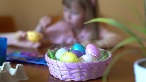 Cute girl paints an Easter egg. Paint on the table. Mom helps her daughter to draw on the egg.