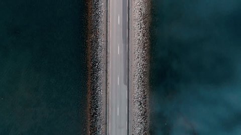 Straight down aerial shot on bridge or rised up road connecting two sides of lake or bay through beautiful blue water. Concept logistics and transportation. Big lorry delivery truck on highway