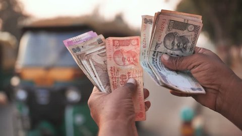 A man recounts Indian rupee money amid tuk tuk.