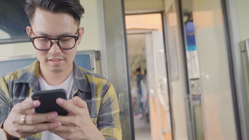 Traveler Asian man using smartphone checking social media while taking a train, Young male tourist backpacker enjoy her journey in Thailand. Lifestyles teen men relax and travel concept. | Shutterstock HD Video #1025891933