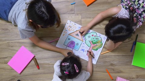 Three children is drawing the picture in the paper on the wooden ground she has many book and color pencil around her, top view of child on floor, Educational concept for school kids