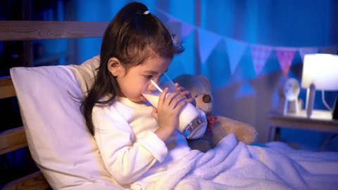 Child asian girl drinking some milk on bed in a dark bedroom at night before sleeping, Comfortable children at home concept