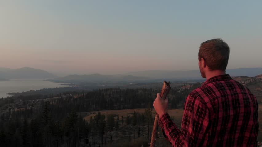 Aerial Drone Shot Pulling Away From Man Standing On Mountain Side Overlooking Valley At Sunset