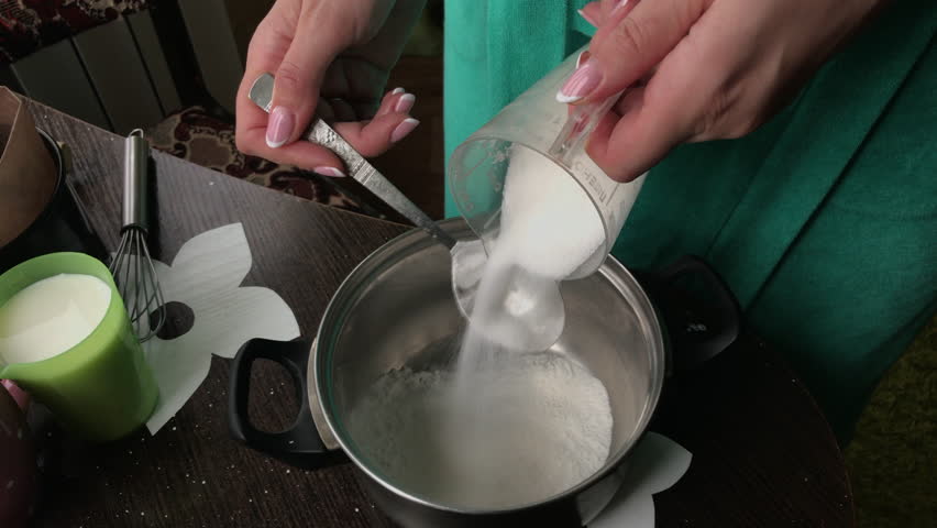 Woman add sugar to food. Cooking a cake of biscuit crumbs and milk jelly. On the surface of the table are the ingredients and cooking utensils.