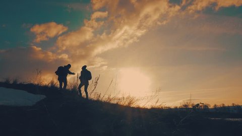 Couple hiking help each other silhouette in mountains. Teamwork couple hiking, help each other, trust assistance, sunset. Man giving hand a woman to help her to climb the mountain.