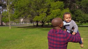 African-american young bald father in striped shirt and jeans holding his little mixed-race boy in his arms and spining him around. Family, joy concept