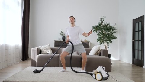 Young Man Having Fun Cleaning House With Vacuum Cleaner Dancing And Using Smartphone.