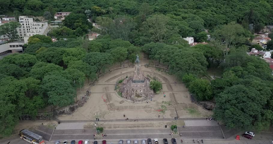 Descending aerial view over monument of General Martin Miguel de Guemes, Salta. Green lush trees surrounding monument.