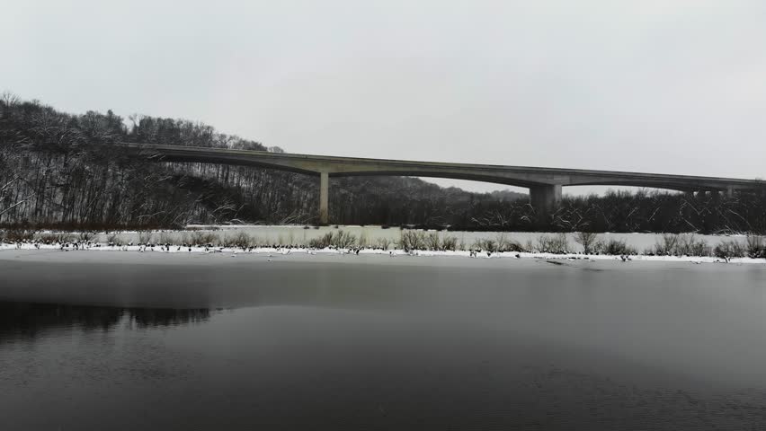 A low aerial shot over a frozen lake towards Page Bridge amid falling snow.