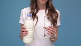 cropped view of girl pouring milk, smiling and showing glass at camera isolated on blue