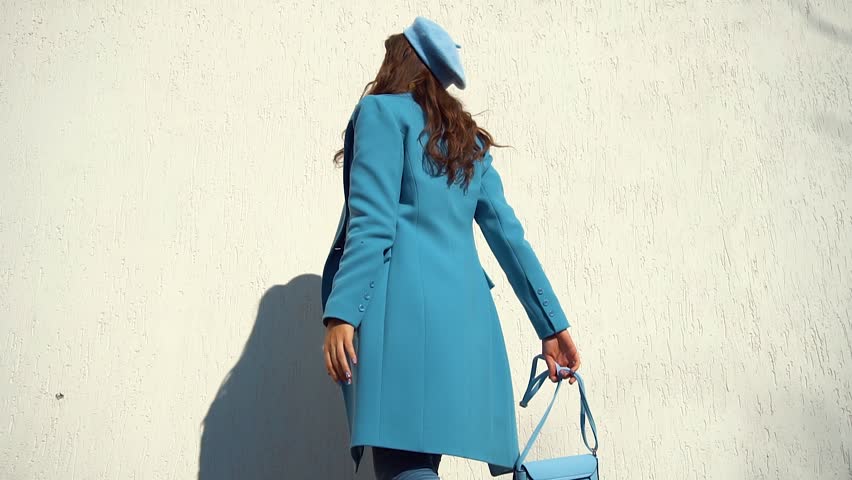 woman posing in a coat on the background of the wall with the handbag