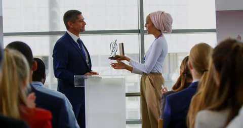 Side view of a Caucasian businessman receiving an award from a businesswoman while the public is applauding him in the business seminar