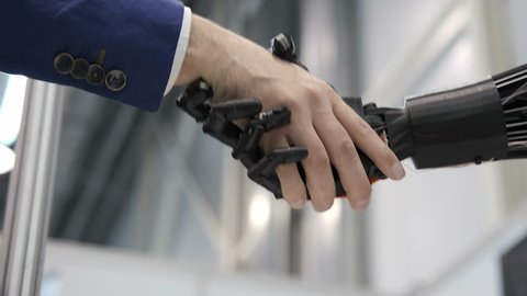 Interaction of man and modern technologies of artificial intelligence. Close up male hand of scientist shakes robotic arm. Robotic and human hands join in a handshake. Meeting and greeting friends