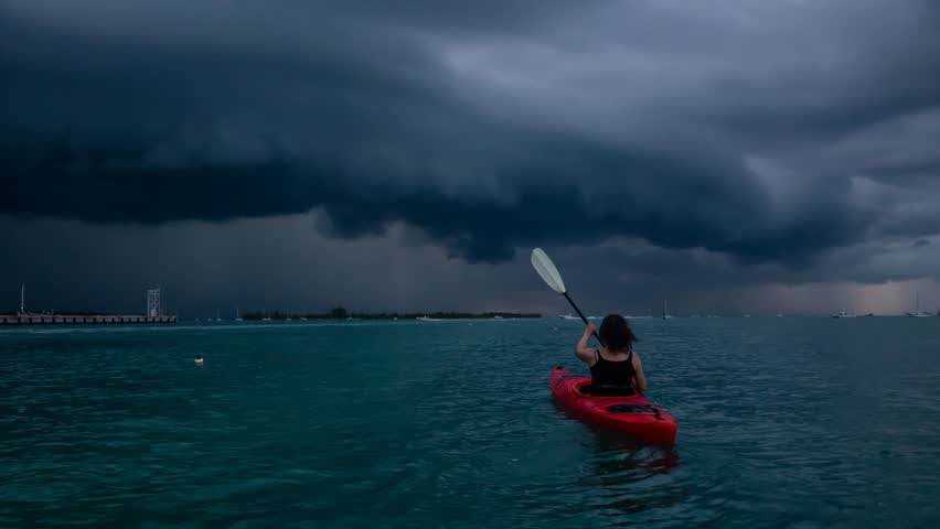 Adventurous girl on a red kayak is kayaking towards a thunderstorm during a dramatic sunset. Taken in Key West, Florida Keys, United States. Still Image Continuous Animation
