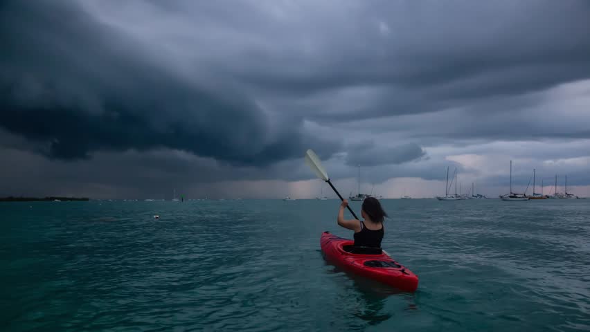 Adventurous girl on a red kayak is kayaking towards a thunderstorm during a dramatic sunset. Taken in Key West, Florida Keys, United States. Still Image Continuous Animation