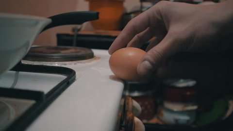 Egg cracked on the edge of a stove with the egg white dripping