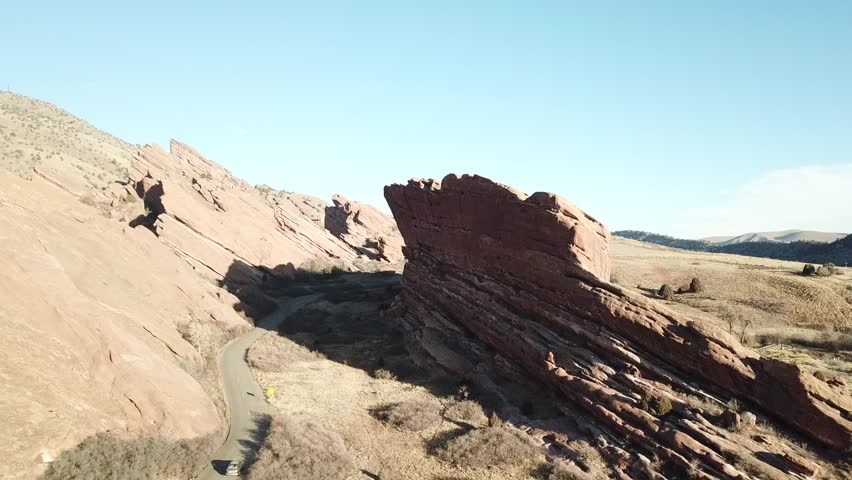 AERIAL: pulling away from a road twisting around a giant boulder in the Red Rocks Park in Colorado.