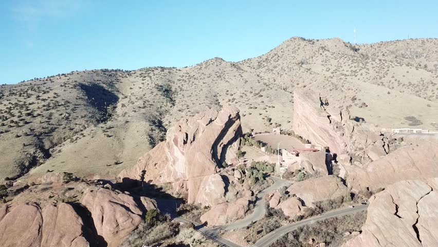 AERIAL: angled push, tilt, and pan to center the amphitheater lost within the giant boulders located at the Red Rocks Park in Colorado.