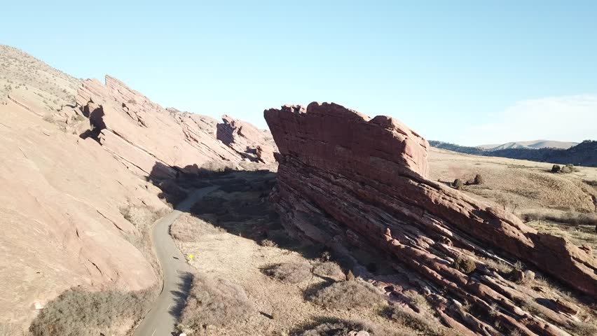 AERIAL: pull and lift away from a road twisting around a giant boulder in the Red Rocks Park in Colorado.