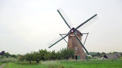 Peaceful Dutch landscape with traditional brick windmill with blades rotating counterclockwise. Typical view of the Holland's countryside in natural lighting