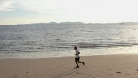 Drone view of Sportive young man running on beach in the morning enjoying freshness and vitality - People healthy lifestyle travel concept- Slow motion 