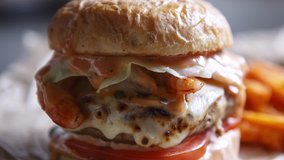 Footage of big tasty burger with sauce,burned cheese & meat served with fried carrot sticks on brown crafted paper in fast food restaurant.Video of fat unhealthy junk food menu in cafe