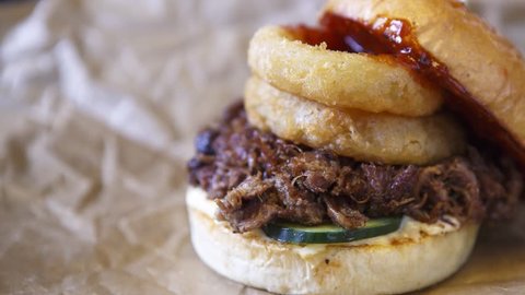 Footage of big tasty exotic burger with fried onion rings, rosted beef meat, cucumber vegetables served on brown paper.Fast food restaurant menu close up.Video of delicious burger fast food