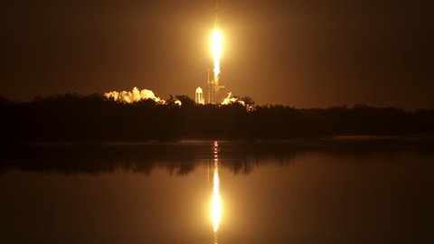 Beautiful reflection on water as a NASA space rocket flies into the night sky from the launch pad at night with flames and fire from the powerful engines. 4K. With sound and slow motion.