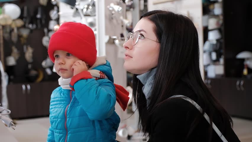 A child, a boy of three, with admiration points his hand at a product in an electrical shop, his mother also admiringly supports her child