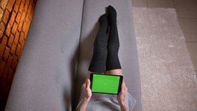 Closeup shoot of female legs in cute socks on the couch indoors. Woman playing video games on the tablet with green chroma screen