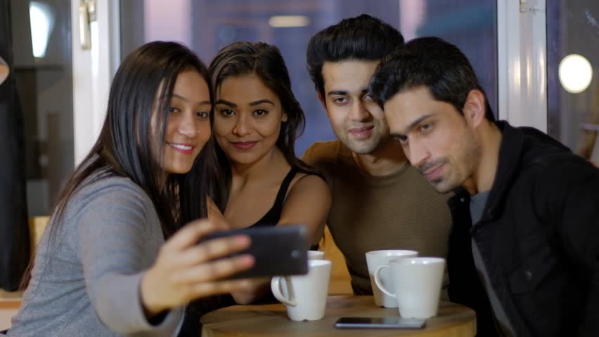 Young friends smile and pout for selfie photos from a mobile phone as they huddle together and then review and discuss about the photo taken and smile