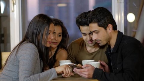 Indian young friends intently look at a mobile screen touch screen and look at something as they share, review and criticize the photo over a coffee together on a cafe talking chatting and talking 