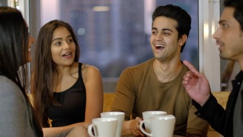 Indian young friends high five and shake hands and congratulate and celebrate their friend over a coffee together on a cafe talking chatting and talking 
