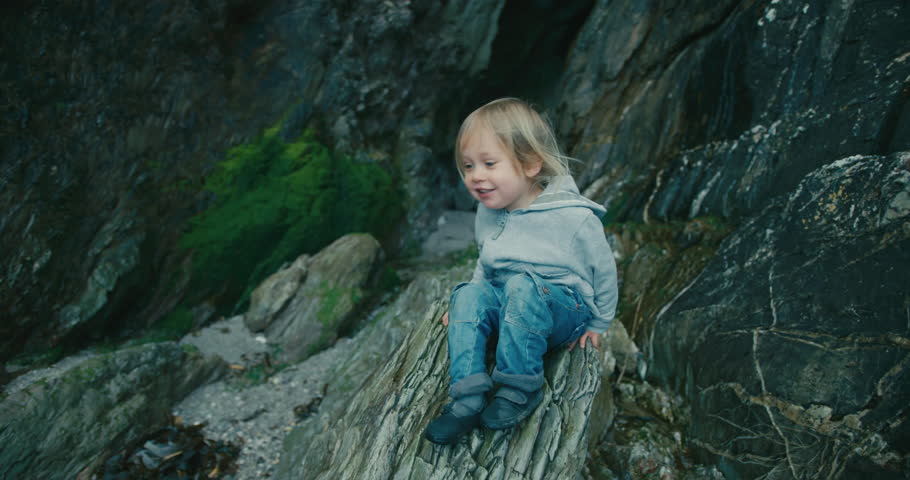A little toddler is sliding down a rock on the beach