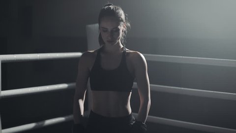 Portrait of tired female boxer standing on the boxing ring and looking intensely at the camera
