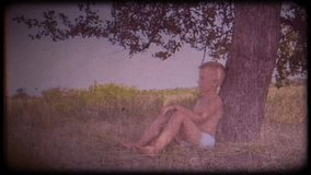 Family video archive. Retro camera 8 mm. Vintage. A little boy sits and dreams under a big tree. Childhood dreams. Place of solitude. Journey back to childhood. Fabulous tree. Memories.  A warm wind