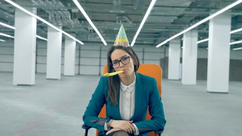 One office worker in a birthday cap blows a whistle, sitting in a chair.