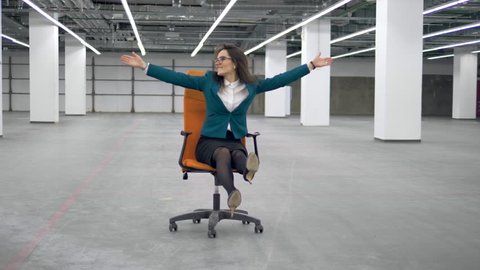 Female worker having fun, riding an office chair.