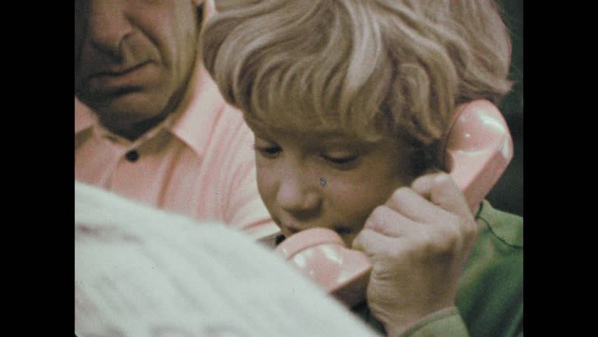 1970s: Man sits at table. Man watches boy talk on telephone. Boy writes in address book. | Shutterstock HD Video #1025986172