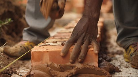 Close up of African builder laying brick on concrete with brown cement mixture