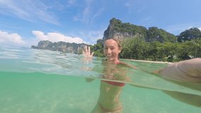 Half in water selfie of young woman having fun on tropical beach in pristine clear water. People travel vacation in exotic destination concept 