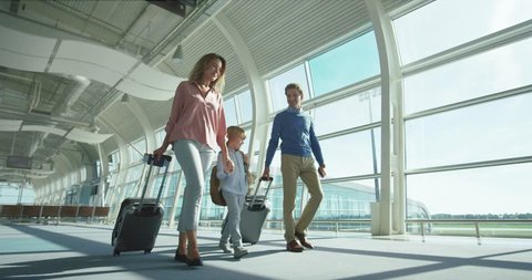 Caucasian parents with small nice son and big suitcases on wheels passing through the camera in the airport passage while going to the departure or arrival gates.